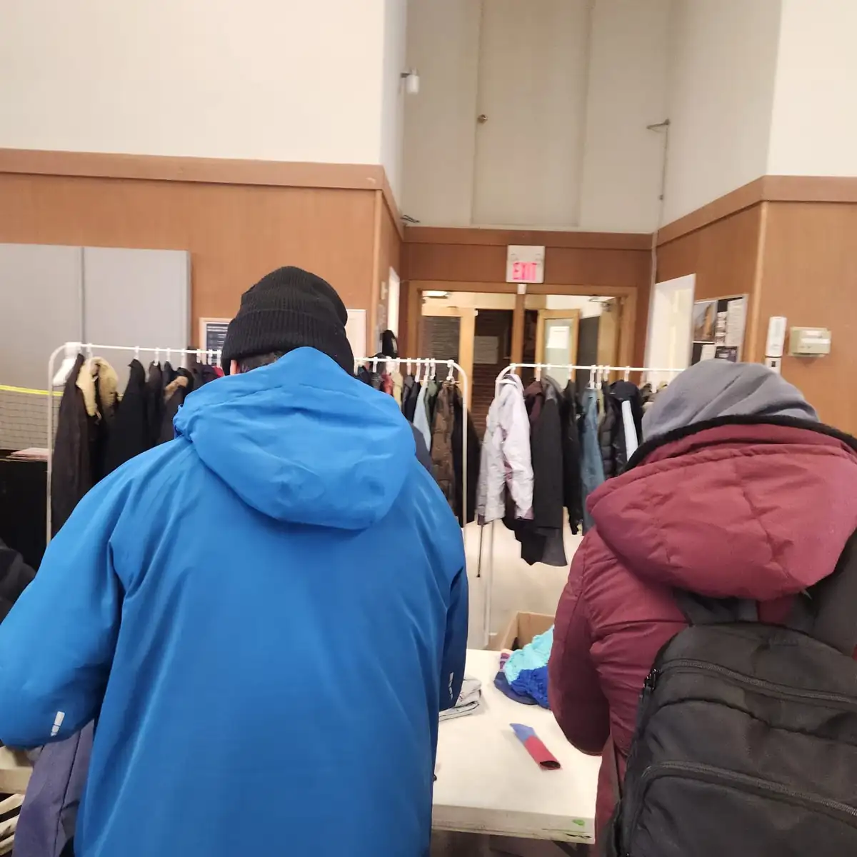 Two people browsing coats on white garment racks at a clothing drive
