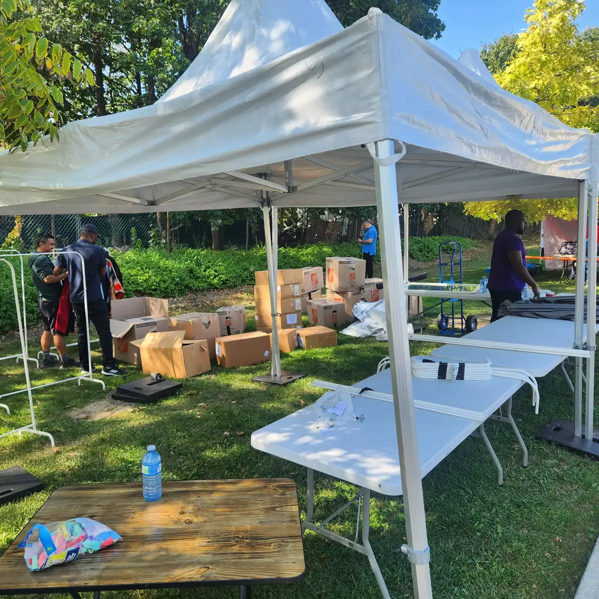 Volunteers organising boxes of donated goods beside clothing racks at a community event