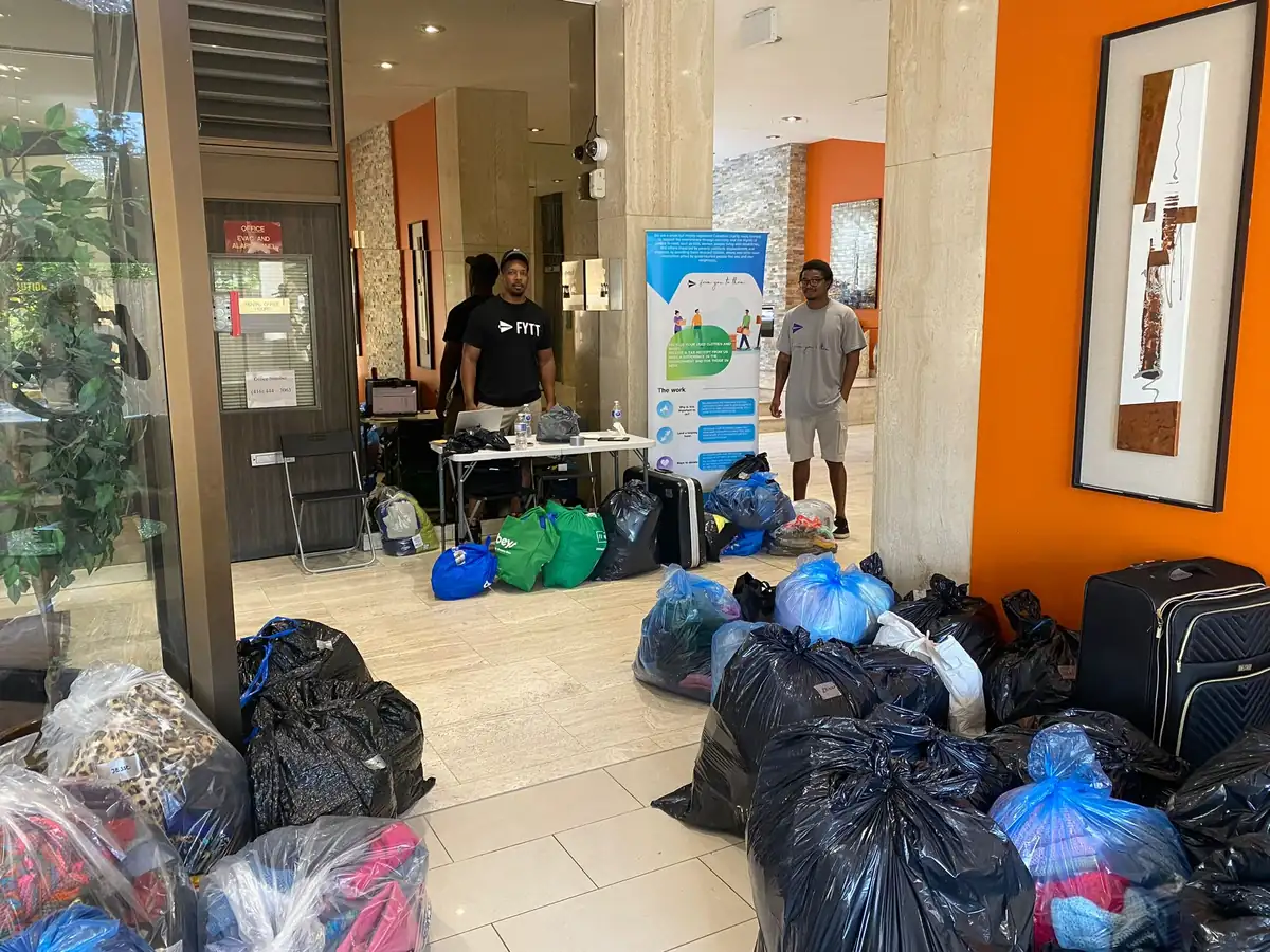Two volunteers behind a table surrounded by bags of donated clothing and shoes