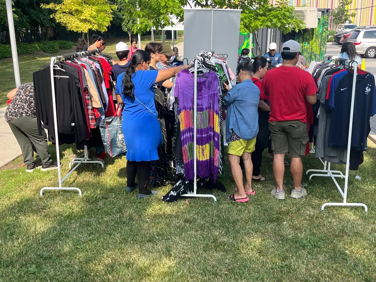Community members browsing clothing racks at a sunny outdoor distribution